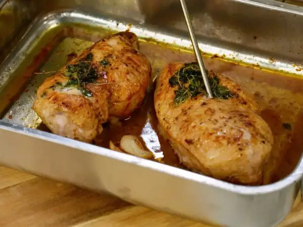 Två saftiga kycklinglårfiléer i en ugnsform, kryddade med örter och vitlök. En termometer mäter temperaturen för perfekt grillad kyckling.