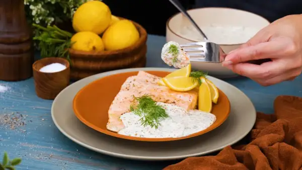 En bit lax med citron och dill, toppad med en krämig klassisk romsås. En gaffel med sås och rom lyfts från skålen.