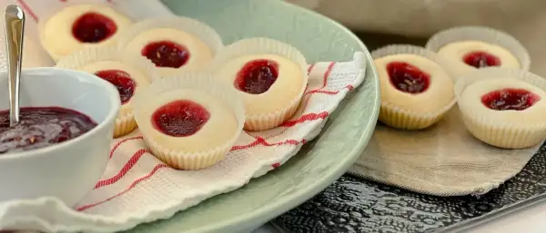 Glutenfria hallongrottor med sylt på en ljusgrön tallrik, bredvid en skål med hallonsylt och en sked.