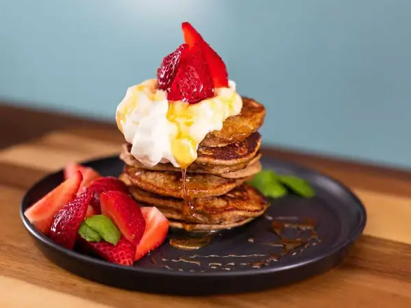 En stapel bananpannkakor med vispgrädde, jordgubbar och sirap. Ett perfekt bananpannkaka recept för frukost eller brunch.